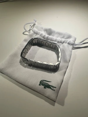 Lacoste silverfärgad armband - Snygg och stilren klocklänk från Lacoste i silverfärgat metallmaterial. Länken har en klassisk design med rektangulära länkar och passar perfekt till din favoritklocka från Lacoste. Kommer i originalpåse med logga.
