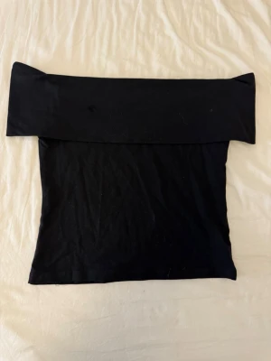 Svart offshoulder topp från Stories - Säljer en svart offshoulder topp från Stories i storlek S (36-38). Toppen har en axelbandslös design med bred kant upptill och är tillverkad i mjukt material som sitter tight mot kroppen. Perfekt för en trendig och stilren look.