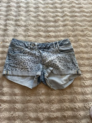 Leopardmönstrade jeansshorts H&M - Säljer ett par ljusblå jeansshorts från H&M med grått leopardmönster och upprullade benslut. Shortsen har fem fickor, bälteshällor och knappgylf. Ena bakfickan har ett randigt mönster för en cool kontrast.