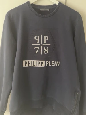 Mörkblå tröja - Cool mörkblå sweatshirt från Philipp Plein med stort tryck och logga framtill. Tröjan har rund halsringning, långa ärmar och ribbade muddar. Materialet känns mjukt och bekvämt, perfekt för en avslappnad streetwear-look.
