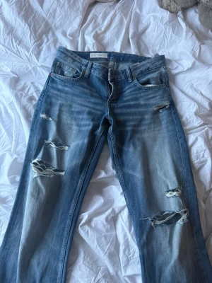 Blå slitna jeans med hål - Säljer ett par blå jeans med snygga slitningar och hål på både lår och knän. 