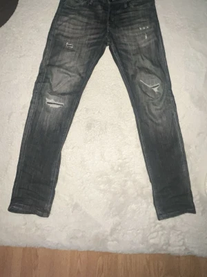 Grå slitna jeans  - Säljer ett par grå skinny jeans med slitningar och hål på båda benen. Jeansen har en tvättad look och klassisk femficksmodell. Perfekta för dig som gillar en avslappnad och trendig stil.