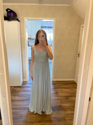 Ljusblå långklänning från Vila - Långklänning från Vila i ljusblå ton med v-ringad front och smala axelband. Överdelen har spetsdetaljer och kjolen är lätt och flödande. Perfekt för dig som vill ha en elegant och stilren look. Materialet känns mjukt och luftigt. Passar perfekt för finare tillfällen som exempelvis bal. Jag är 166 cm som referens.