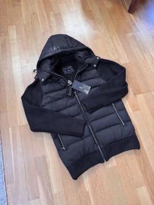 Leon Marcel Hybridjacka – Midnight Navy | Avtagbar Luva | Ny Med Prislapp - Ny med prislapp — Leon Marcels hybridjacka i djup midnattsblå med quiltad pufferkropp och stickade ärmar. Avtagbar luva och lyxiga microfleecefickor som håller händerna varma — detaljer som gör skillnad. Tidlös Skandinavisk design som passar till allt. Perfekt för höst/vår/vinter och kyliga vårdagar. Säljer direkt för ett bättre pris än butik. 📦 Spårad frakt, väl förpackad.