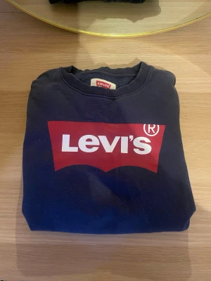 Mörkblå sweatshirt från Levi's - Säljer en mörkblå sweatshirt från Levi's med det klassiska röda och vita logotrycket på bröstet. Tröjan har rund halsringning och ribbade muddar vid ärmar och nederkant. Perfekt för en avslappnad och stilren look.skriv för fler bilder. Pris kan diskuteras!💗