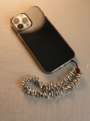 Handgjord Mobilstrap / Mobilsmycke – Silverfärgade Metalldetaljer - Ge din mobil en lyxig och personlig touch med detta handgjorda mobilsmycke. Denna mobilstrap är tillverkad med snygga silverfärgade detaljer och en diskret röd accent som ger en unik karaktär. 