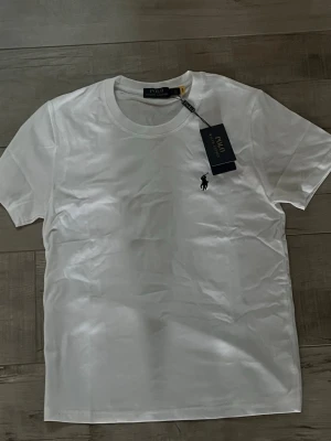 Vit Ralph lauren T-Shirt - En ny T-shirt från Ralph lauren med tag! Storleken är S men jag skulle säga mer XS och passar bäst runt 170. Kontakta om intresse! Obs: pris ej hugget i sten så kom inte med orimliga prisförslag tack!