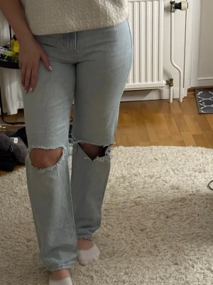 Ljusblå ripped straight leg jeans - Säljer ett par ljusblå jeans från Gina med raka ben och stora slitningar över knäna. Jeansen har en avslappnad passform och klassisk femficksdesign. Perfekta för en trendig och avslappnad stil. Materialet är denim i bomull. Strl 36.