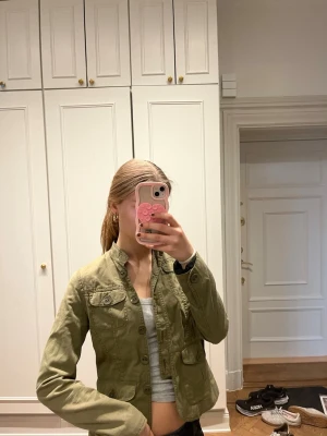 Olivgrön overshirt med fickor - Säljer en olivgrön militär overshirt med klassisk krage och knäppning framtill. Jackan har två bröstfickor med lock och två sidofickor. Materialet är bomull och modellen är rak med en något kortare passform. Perfekt för lager-på-lager och snygg till jeans.