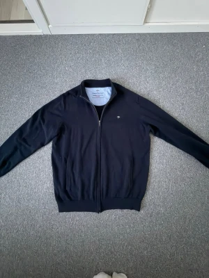 Marinblå ziptröja från Peak Performance - Snygg marinblå ziptröja från Peak Performance med liten logga på bröstet. Tröjan har hög krage, dragkedja hela vägen och ribbade muddar vid ärmslut och nederkant. Perfekt att slänga på sig över en t-shirt för en avslappnad look.