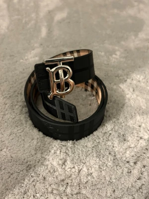 Snygg Svart-beige med B-spänne  - Snyggt vändbart bälte med klassiskt rutmönster på ena sidan och svart på andra. Bältet har en stor metallspänne. Perfekt accessoar för att lyfta din outfit.