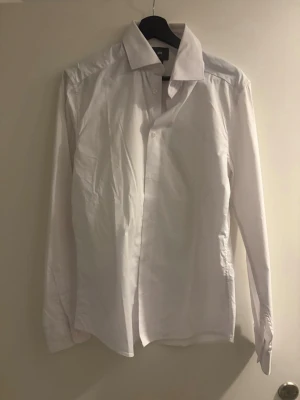 Klassisk vit skjorta från H&M - Säljer en klassisk vit skjorta från H&M med lång ärm och knappar framtill. Skjortan har en tidlös design med normal passform och är tillverkad i bomull, perfekt till många olika stilar.