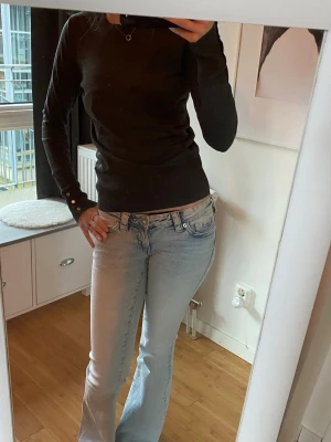 Mörkgrå stickad tröja med knappar - Mysig mörkgrå stickad tröja med rund halsringning och långa ärmar. Tröjan har ribbade muddar och dekorativa knappar vid ärmsluten som ger en snygg detalj. Använd få gånger