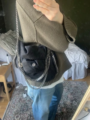 Svart Stella McCartney Falabella väska - Säljer en svart Stella McCartney Falabella handväska i veganskt mockaliknande material. Väskan har silverfärgade kedjedjor som ej rostat. Väskan är rymlig och du får plats med en 15tums dator i. Måtten är 37x36x9. Perfekt som vardagsväska eller till festligare tillfällen. Innertyget är lite smutsigt men annars är väskan i fint skick. Dustbag tillkommer. Tveka inte på att skriva om ni har ytterligare frågor eller prisförslag❤️