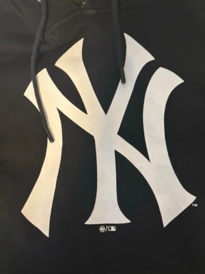 Svart Yankees hoodie från '47 - Säljer en svart hoodie från '47 med stor vit New York Yankees-logga på bröstet. Hoodien har huva med dragsko och är tillverkad i mjukt material som passar perfekt för en avslappnad streetwear-look.