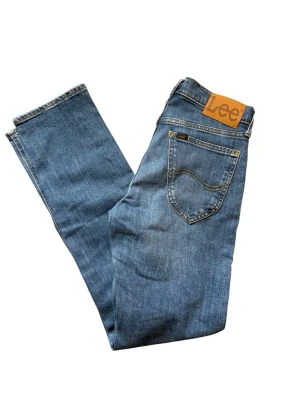 Herr blå jeans från Lee - Snygga ljusblå Lee-jeans med klassisk design. Rak passform och normal midja. Knäppning fram och Lee-logga på bakfickan. Väldigt bra skick i storlek W28/L32.