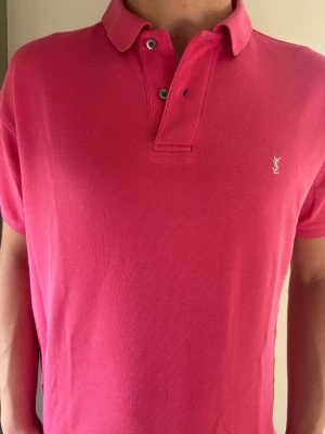 Exklusiv Yves Saint Laurent (YSL) Pikétröja | Strl M  - Exklusiv rosa pikétröja från Yves Saint Laurent. Perfekt färgklick för våren och sommaren som ger en lyxig stil.  🧵 Märke & Modell: YSL - Kortärmad Piké 📏 Storlek & Passform: Storlek M. Sitter snyggt! Modellen är 189 cm. 🧩 Material: 100% bomull av högsta premiumkvalitet. ✅ Skick: 8/10 - Mycket fint skick, lite text på nacketiketten och en väldigt liten knut på baksidan.  💰 Nypris: ca 3500 kr i butik. ‼️ Skickas samma dag/senast dagen efter ‼️ 