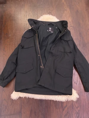 Svart Fieldjacket från Brandit - Säljer nu en riktigt fet fieldjacket från brandit med fyra stora fickor framtill och dragkedja. Jackan har hög krage med snörning och knappdetaljer vid fickorna. Perfekt nu inför våren och jag säljer om vanligt väldigt billigt. Jackan är i storlek 158/164 men passar dig som är 170-176 typ. Kom dm med prisförslag och fler frågor elelr bilder!