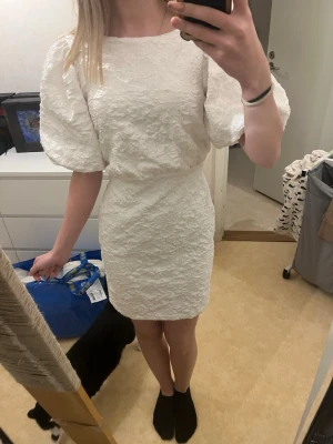 Student klänning - Säljer en jätte fin vit student klänning med puffigt blom mönster, rosett och dragkedja där bak och fina eleganta armar. Använd och tvättad EN gång. Inga fel på den, den är hel och perfekt. Den är lite stor i storlek så den passar mot S kanske M också. Den har tre lager (2 vita och sen 1 vitt med mönstret) 
