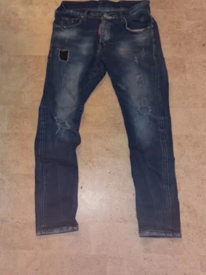 Dsquared 2 Jeans  - Säljer ett par blå jeans med slitningar. Jeansen har klassisk femficksmodell, normal midja och raka ben. Materialet är denim och de har en tvättad, lite vintage look. Perfekta för dig som gillar en avslappnad och trendig stil.