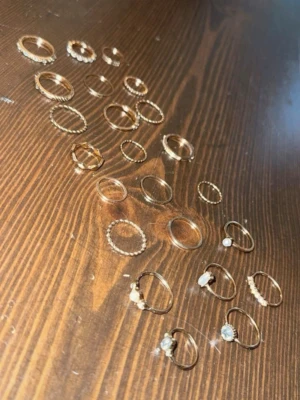 Set med guldfärg i ringar med pärlor - Säljer ett set med flera tun pushingar i guldfärg, vissa dekorerade olika st/bitar, pärlor och små havingar. Ringarna har olika former och detaljer, vissa med stenar och andra med pärlor för en trend bars look. Perfekt för att mixa och matcha på olika recurring. MASSA OLIKA STORLEKAR, 24 st🥹🧸🩷