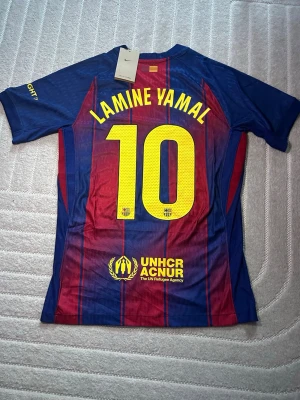 FC Barcelona matchtröja Lamine Yamal - Säljer en officiell FC Barcelona matchtröja från Nike med Lamine Yamal och nummer 10 på ryggen. Tröjan är blå och röd med gula detaljer, klubbmärke och sponsorloggor på bröstet. Tillverkad i lätt och ventilerande material, perfekt för fotboll eller träning.