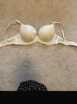 Vit push-up bh med spetsdetaljer - Snygg vit bh med vadderade kupor och bygel för extra stöd. Bh:n har fina spetsdetaljer på sidorna och justerbara axelband för bästa passform sopm gör den både bekväm och stilren. Perfekt för dig som vill ha en enkel men elegant bh.