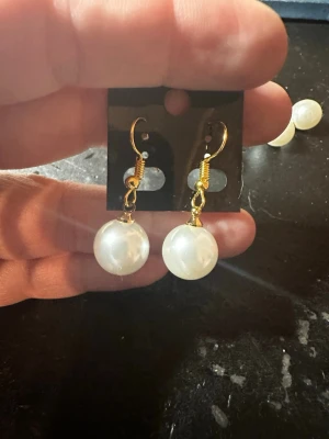 Guldörhängen med stora pärlor - Snygga örhängen med stora vita pärlor och guldfärgade krokar. Klassisk rund form som ger en elegant touch till din stil. Perfekta för dig som gillar statement-smycken och vill sticka ut lite extra.