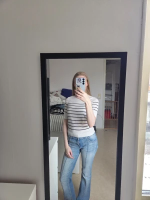 Vit randig topp med kort ärm - Säljer en vit topp med svarta horisontella ränder. Toppen har rund halsringning och korta ärmar. Materialet känns mjukt och stretchigt, troligen bomull eller en bomullsblandning. Passformen är normal och toppen är enkel men stilren.