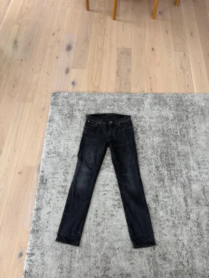Svarta nudie slim fit jeans - Snygga svarta slim fit jeans med klassisk femficksdesign och dragkedjegylf. Jeansen har en smal passform och är tillverkade i ett stretchigt denimtyg som sitter skönt hela dagen. Har en liten lagning i skrevet som du kan se på sista bilden