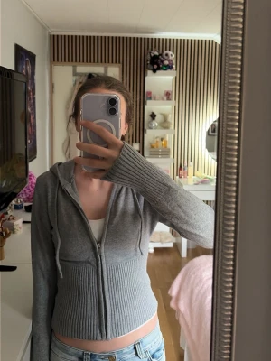 Grå hoodie från Gina Tricot  - Snygg grå croppad hoodie med dragkedja och huva. Tröjan har långa ärmar med breda ribbade muddar och dragsko i huvan. Perfekt för en chill och avslappnad stil. Passar till jeans eller leggings. Dragkedjan kan vara lite svår att stänga men fungerar ändå som den ska❤️
