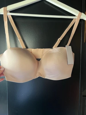 Beige bh med avtagbara band - Snygg beige bh med avtagbara och justerbara axelband. Bh:n har släta kupor och bygel för extra stöd. Perfekt under ljusa toppar tack vare den diskreta färgen. Materialet känns mjukt och stretchigt mot huden.