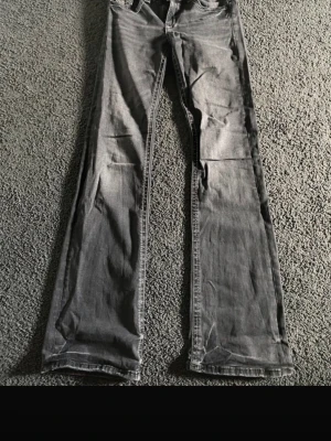Grå bootcut jeans med låg midja - Säljer ett par gråa bootcut jeans med låg midja och klassisk femficksdesign. Jeansen har en lätt tvättad look och raka ben som släpper ut lite vid anklarna. Perfekta för dig som gillar en avslappnad och trendig stil.