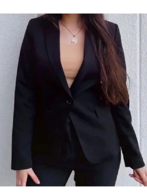 Svart klassisk kavaj från Mango - Snygg svart kavaj med smal passform och klassisk krage. Kavajen har två knappar framtill och diskreta fickor. Perfekt för en stilren look och enkel att matcha med olika outfits. Materialet ser ut att vara en blandning av polyester och viskos. Aldrig använd!