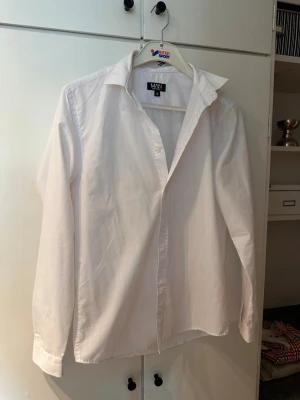 Vit skjorta  - Klassisk vit skjorta med lång ärm och krage. Skjortan har knappar framtill och är tillverkad i ett mjukt bomullstyg. Perfekt för en clean och stilren look.