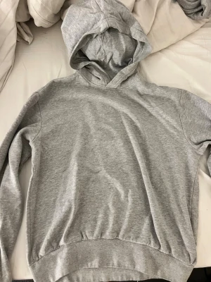 Grå basic hoodie med huva - Enkel och stilren grå hoodie med huva och långa ärmar. Tillverkad i mjukt material, perfekt för en avslappnad look. Klassisk passform utan tryck eller detaljer.