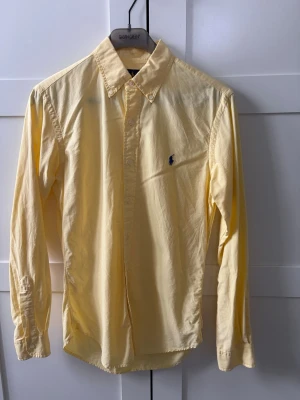 Gul skjorta från Ralph Lauren - Klassisk gul skjorta från Ralph Lauren i slim fit-modell. Skjortan har en stilren design och är tillverkad i ett lätt material som passar perfekt till många olika outfits.