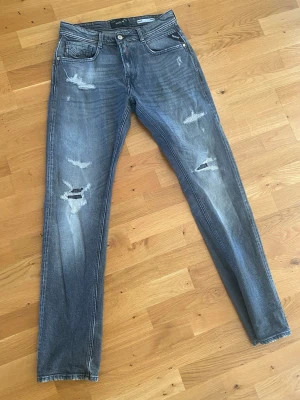 Grå slitna jeans från Replay - Säljer ett par grå Replay jeans med slitningar och distressed detaljer på både fram- och baksida. Nypris 2200 kr och storlek 28/32. Modell Rocco comfort fit