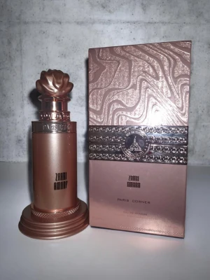 Zahi Amara från Paris Corner - Lyxig parfym i en roséguldfärgad flaska med elegant, dekorativ kork och matchande ask. Flaskan har en stilren, metallisk finish och tydlig logga. Perfekt för dig som gillar exklusiva dofter och snygg design på parfymflaskan.
