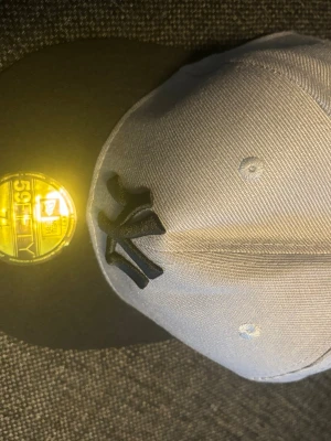 New Era 59FIFTY NY keps grå/svart - Snygg New Era 59FIFTY keps i grått med svart skärm och broderad New York Yankees-logga framtill. Klassisk flatbrim-modell med guldigt klistermärke på skärmen. Perfekt accessoar för streetwear-stilen.