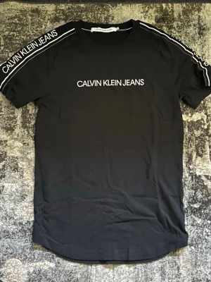 Svart Calvin Klein Jeans t-shirt - Svart t-shirt från Calvin Klein Jeans med vit logga på bröstet och längs båda axlarna. Klassisk rund halsringning och korta ärmar. Tillverkad i mjuk bomull för en bekväm känsla och snygg passform.
