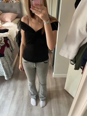 Svart offshoulder topp med twist - Snygg svart offshoulder topp med twistdetalj framtill. Toppen är tight och har en croppad känsla, perfekt för att lyfta din outfit. 