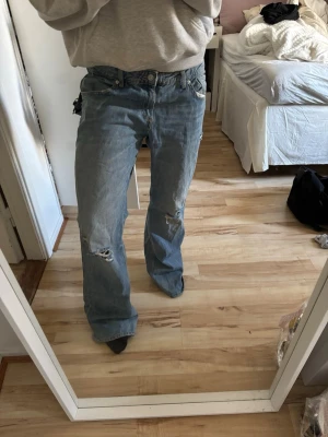 Ljusblå slitna bootcut jeans Zara  - Säljer ett par ljusblå bootcut jeans med slitningar och hål på knäet. Jeansen har klassisk femficksdesign och är tillverkade i denim. Perfekta för en avslappnad och trendig look.