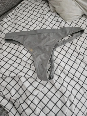 Grå stringtrosa i bomull - Säljer en enkel grå stringtrosa i mjuk bomull med klassisk låg midja och smala sidor. Perfekt för dig som gillar minimalistisk stil och bekväma material. Inget synligt märke.