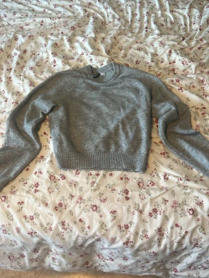 Grå stickad tröja från Divided H&M - Mysig grå stickad tröja från Divided H&M med rund halsringning och ribbade muddar vid ärmslut och nederkant. Perfekt för lager-på-lager och enkel att matcha med jeans eller kjol. Klassisk och stilren modell som passar till mycket.
