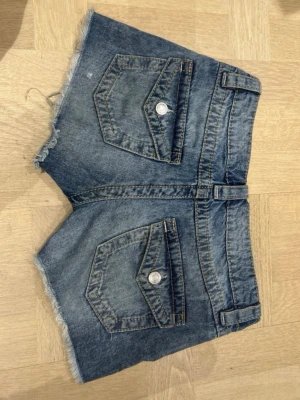 Blå jeansshorts - Säljer ett par blå jeansshorts från Gina tricot i storlek 158. Shortsen har två stora fickor bak med lock och knapp, samt klassiska fickor fram. Perfekta för sommaren!🩵🪽