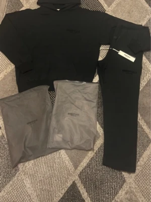 Svart Essentials hoodie med huva - Säljer en svart hoodie från Essentials med huva och känguruficka framtill. Hoodien har diskret Essentials-logga på bröstet och är gjord i mjukt material, perfekt för en avslappnad streetwear-look.