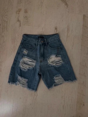 Blåa högmidjade jeansshorts med slitningar - Blå jeansshorts med hög midja och slitna detaljer framtill. Ny utan prislapp 