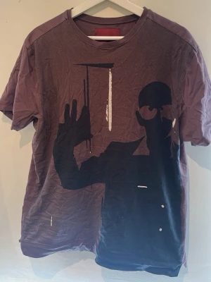 LIMITATO t-shirt - Cool brun t-shirt från LIMITATO med ett stort svart konstnärligt tryck framtill som föreställer en siluett. T-shirten har rund hals och korta ärmar, perfekt för en avslappnad och trendig look. Efter en strykning på T-shirten kommer den se mkt bättre utt därav pris  litet hål vid armhåla som köparen vet om