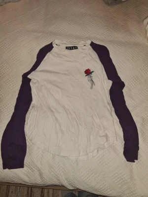 Vit och lila långärmad topp från Istay - Vit långärmad topp från Istay med lila ärmar och en broderad detalj av en skelett hand som håller en röd ros på bröstet. Klassisk basebollmodell med rund halsringning.
